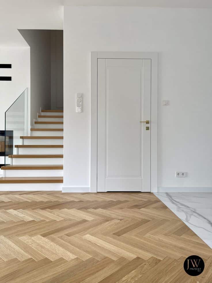 Modern interior with a wooden herringbone floor, white door, and floating staircase for minimalist home design.