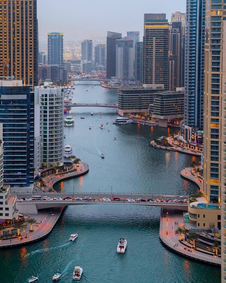 Aerial view of boats navigating the Dubai Marina, surrounded by modern skyscrapers and a bridge at dusk.