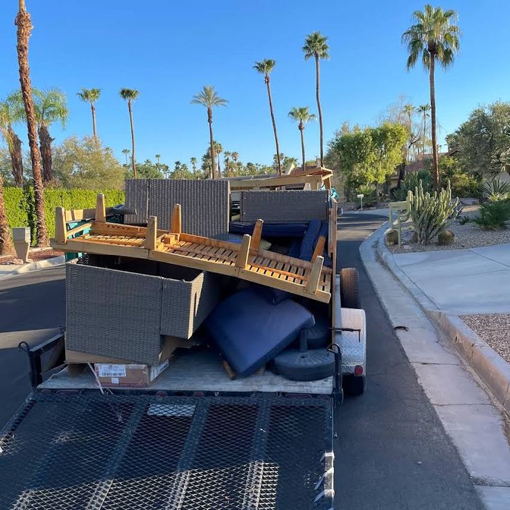 Loaded truck with outdoor furniture on a sunny street lined with palm trees.