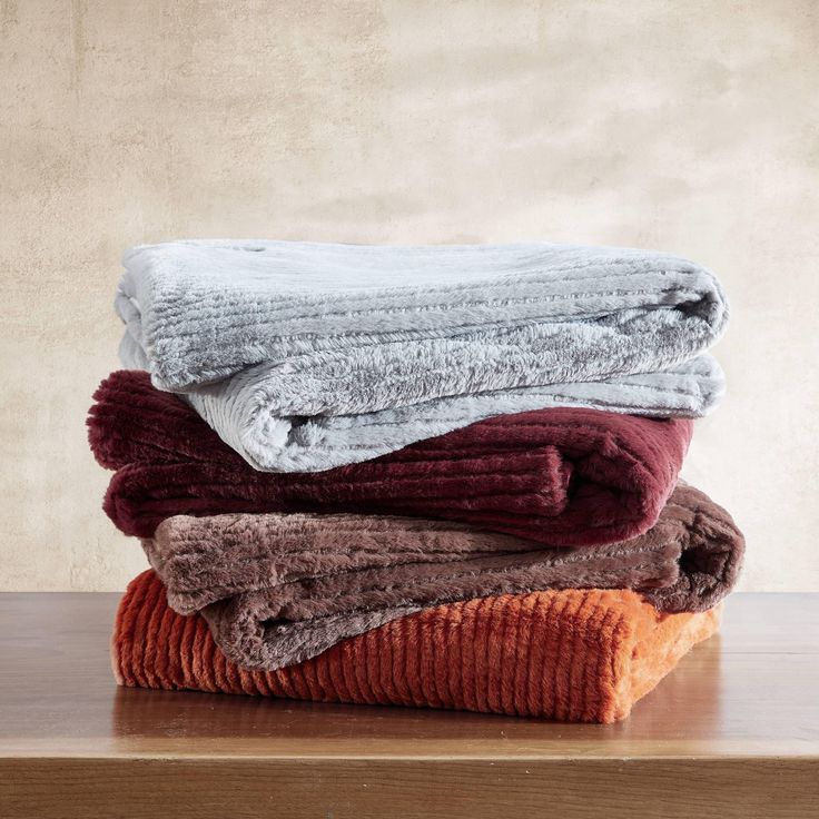 Stack of cozy blankets in gray, burgundy, brown, and orange on a wooden table, perfect for home decor or warmth.