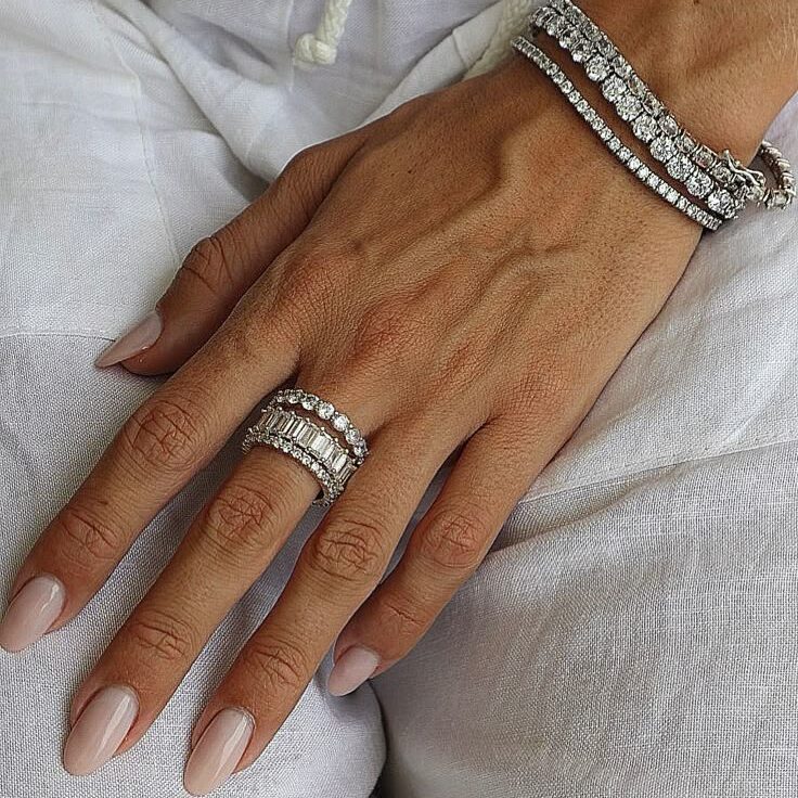 Elegant hand adorned with diamond bracelets and rings on white fabric background.