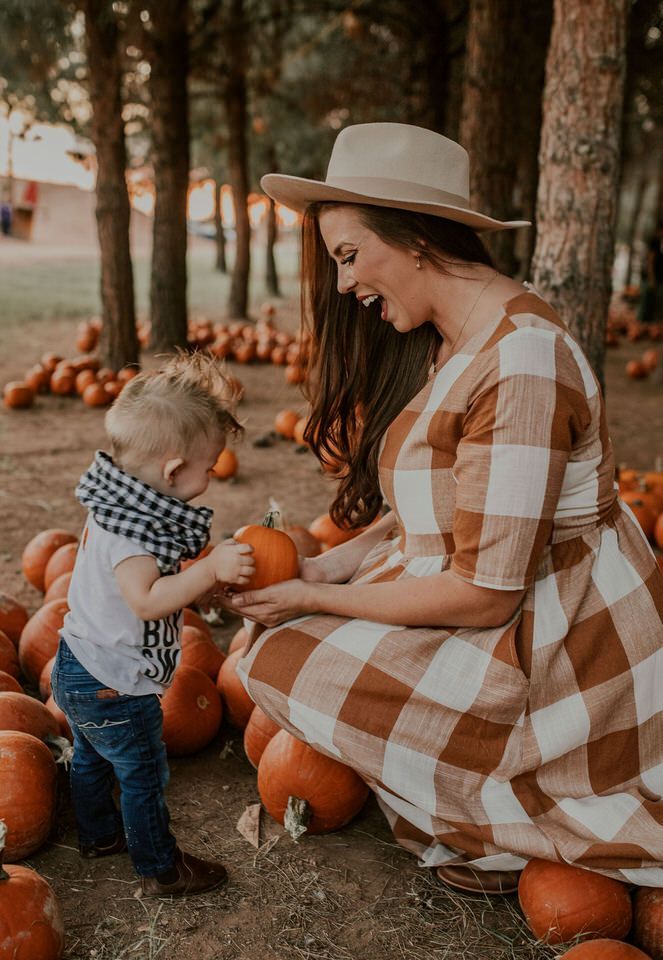 Mom and child enjoy a pumpkin patch moment, surrounded by pumpkins and trees, in warm autumn attire.