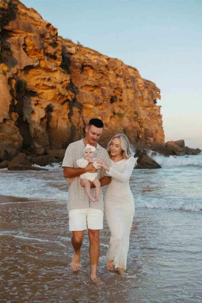 Family walking on a beach near cliffs at sunset, enjoying a serene coastal moment by the ocean.