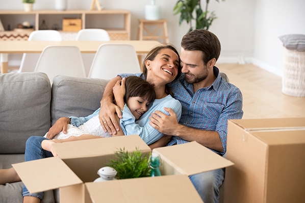 Happy family embracing on a couch in their new home surrounded by moving boxes.