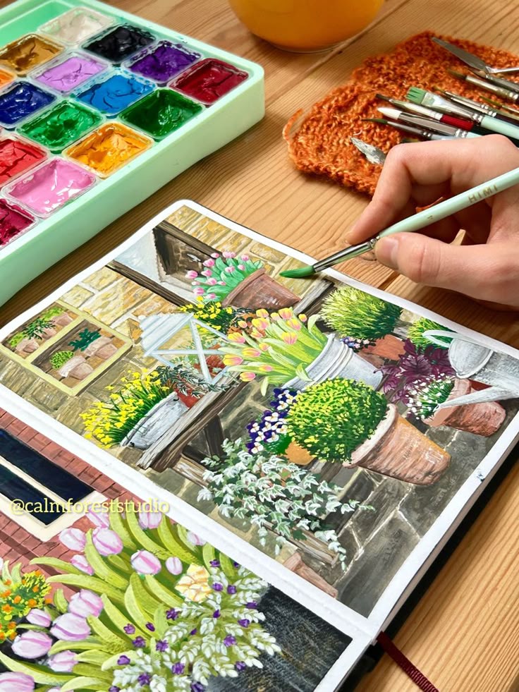 Artist painting a vibrant garden scene with watercolors in a sketchbook on a wooden table.