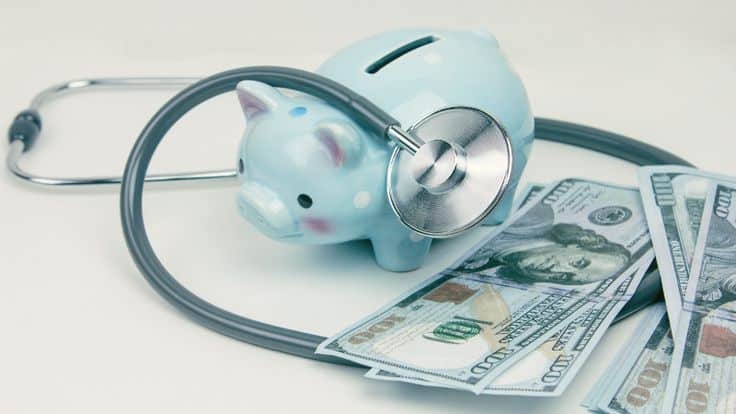 Blue piggy bank, stethoscope, and US dollar bills symbolize financial health and savings.