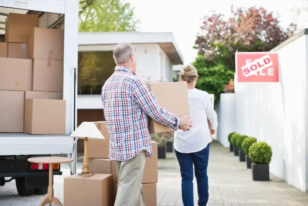 GettyImages-135385177 Couple moving boxes into a new home with a sold sign, symbolizing a successful property purchase. | Sky Rye Design Couple moving boxes into a new home with a sold sign, symbolizing a successful property purchase.