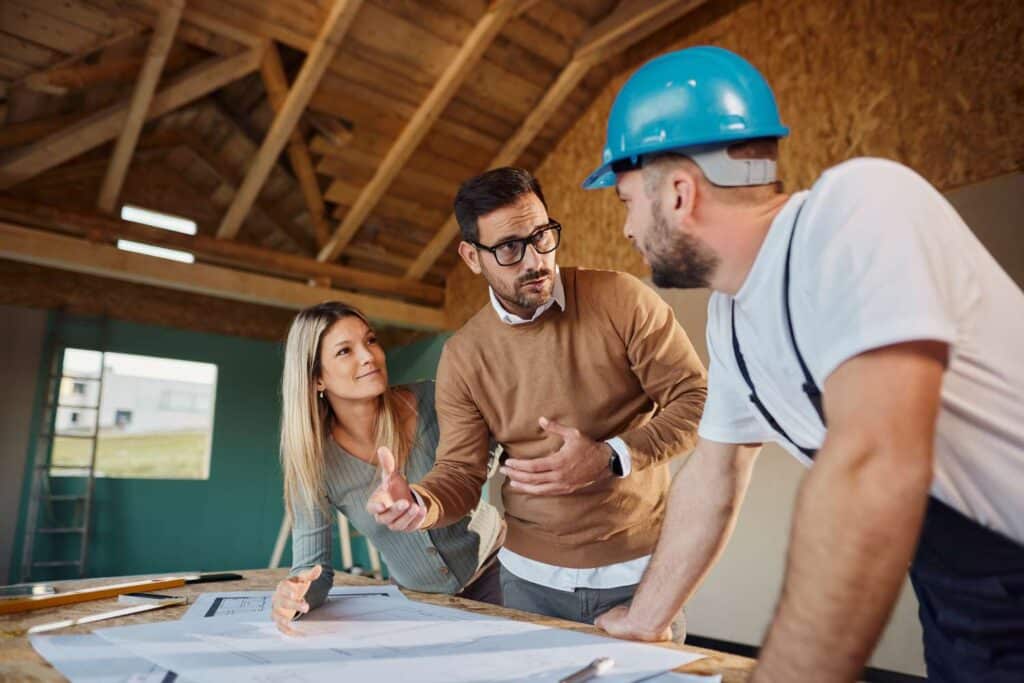 Architects discuss construction plans with a contractor in a partially built wooden house.