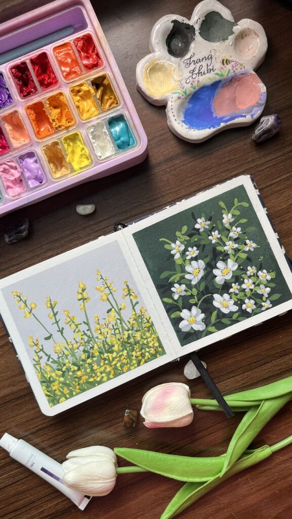 Watercolor flowers with paint palette and pastel tulips on a wooden table.