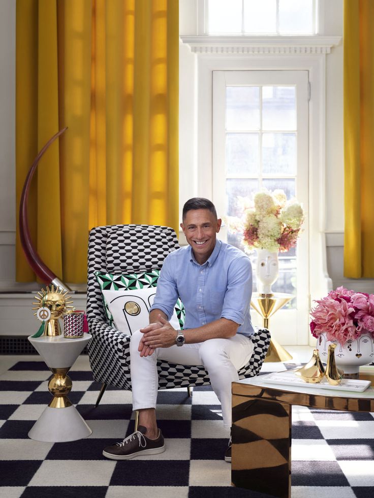 Man in stylish living room with bold patterns, gold accents, and vibrant decor elements.