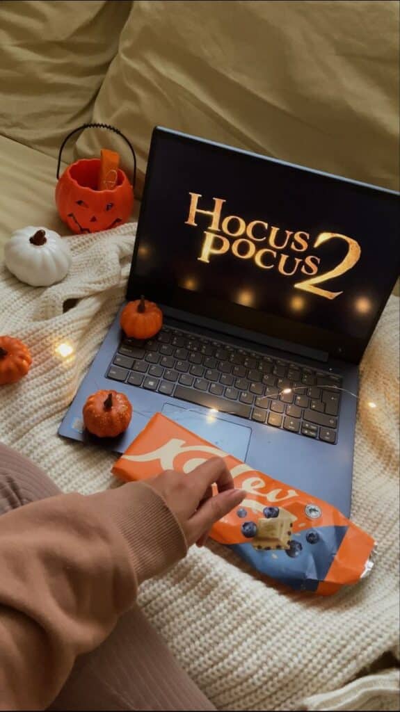 Cozy movie night with Hocus Pocus 2 on laptop, surrounded by pumpkins and snacks on a blanket.