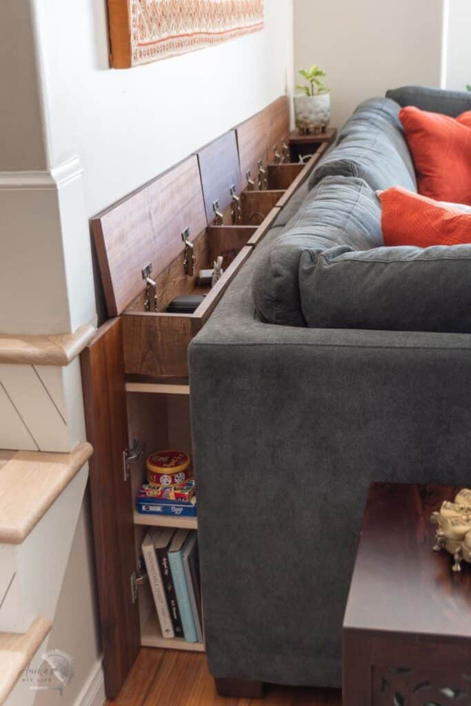 Gray sectional sofa with built-in wood storage compartments and orange cushions in a cozy living room setting.