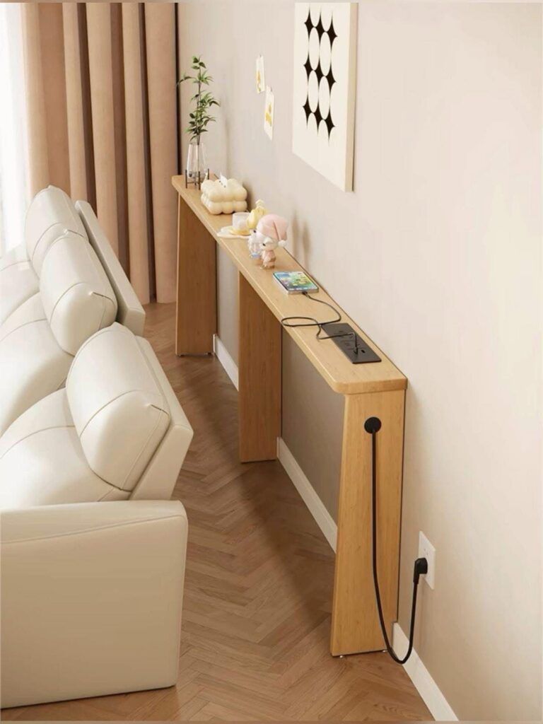 Minimalist console table behind sofa with decor and charging station on wooden herringbone floor.