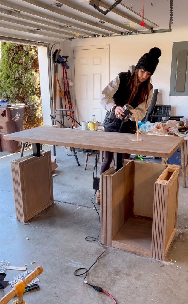 Person assembling wooden furniture in a garage workshop, pouring glue on a table surface.