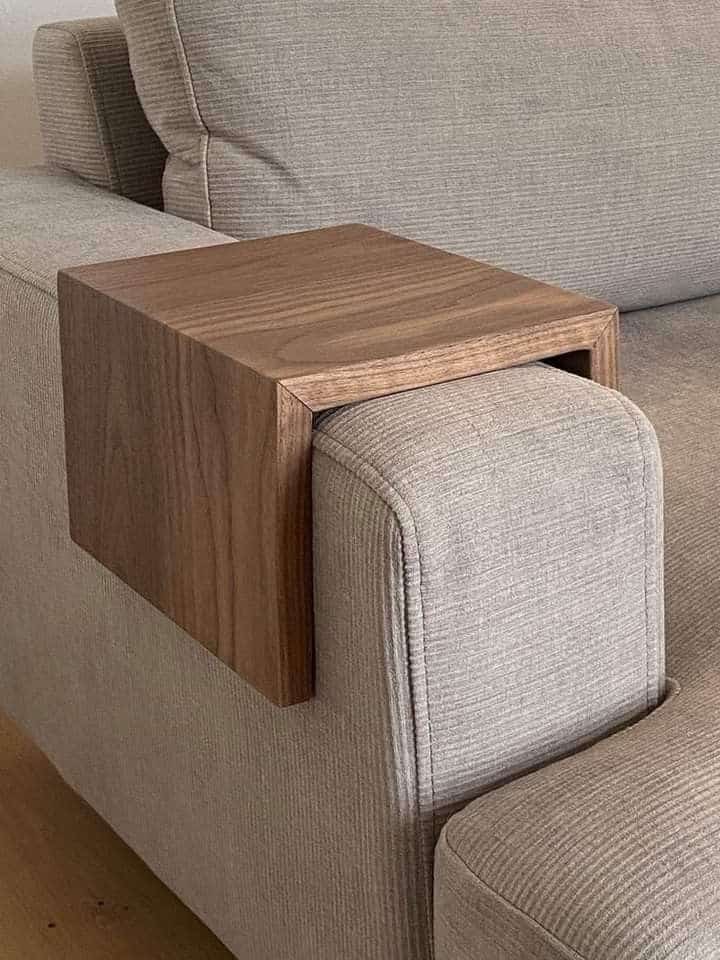 Wooden armrest table on beige couch, perfect for holding drinks and snacks. Handy and stylish living room accessory.