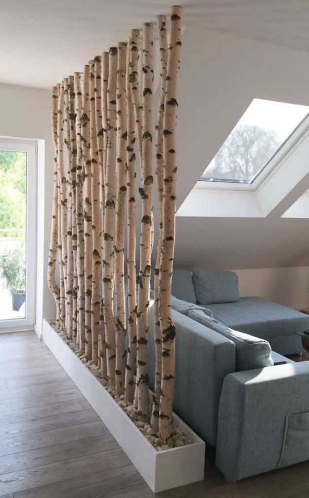 Birch tree room divider in modern living space with skylight and blue sofa.