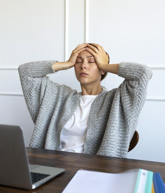Stressed woman at desk with laptop, holding head in hands, feeling overwhelmed.