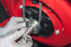 Gloved hands adjusting a belt pulley on a red machine, demonstrating mechanical maintenance and repair process.