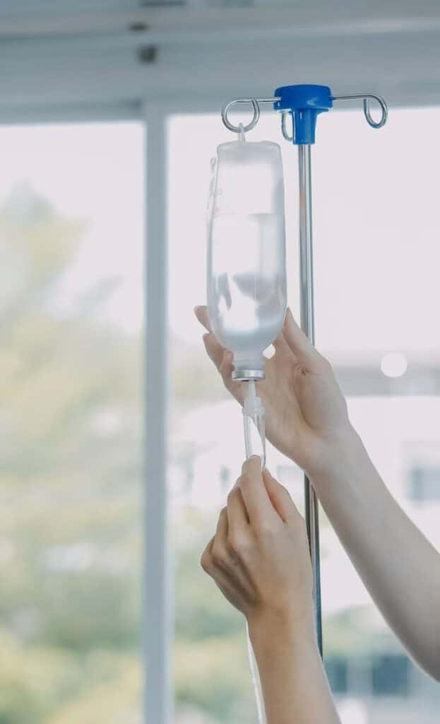 Hands adjusting an IV drip in a hospital setting, providing medical care and hydration therapy.