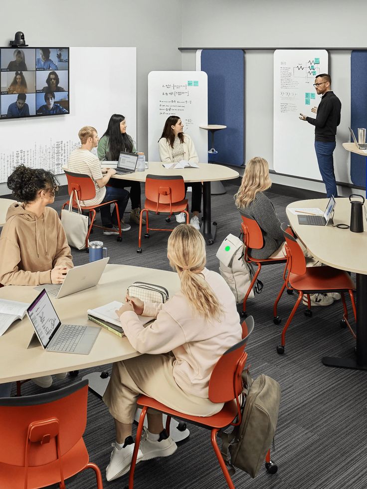 Classroom setting with diverse students and a teacher, using hybrid learning with digital and physical resources.