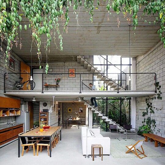 Spacious modern loft with open-plan design, industrial elements, and lush greenery, featuring a mezzanine and staircase.