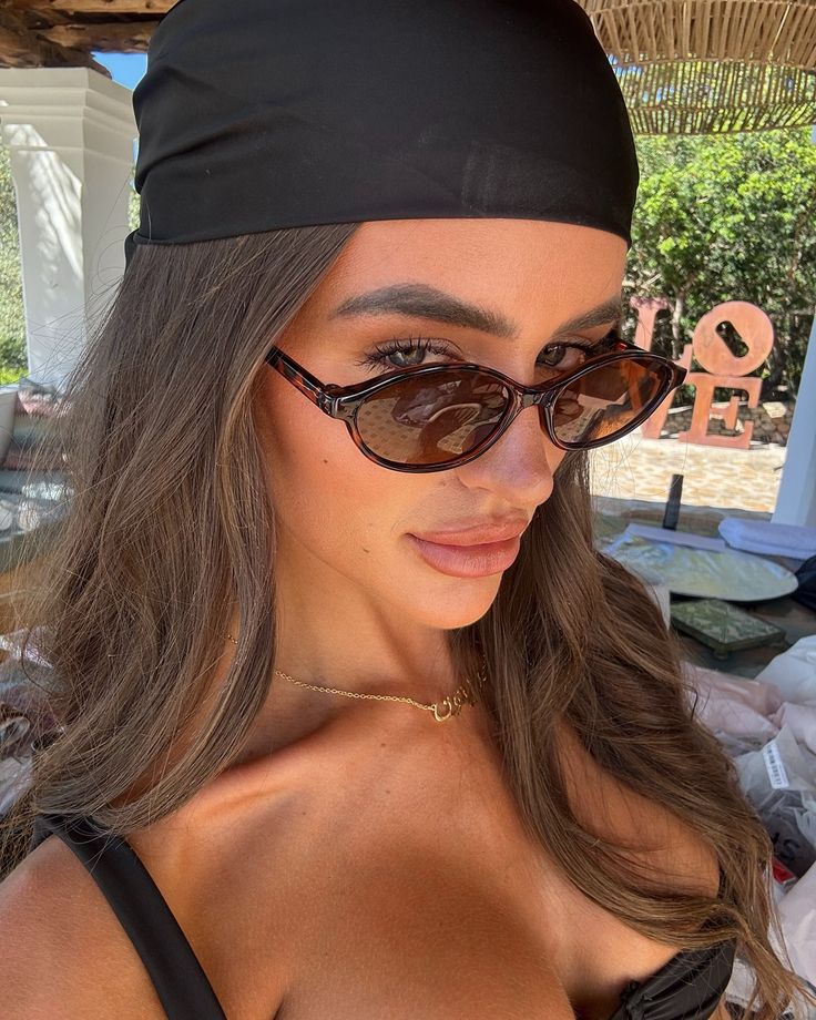 Woman with sunglasses and black headscarf outdoors, close-up portrait in sunny setting.