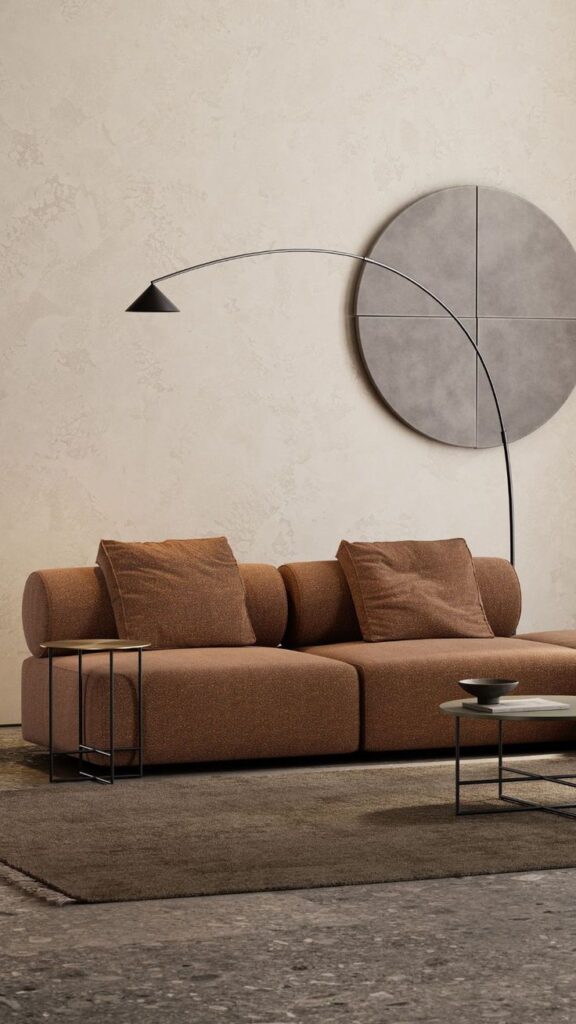 Modern living room with brown sofa, sleek arc floor lamp, round wall art, and minimalist coffee tables.