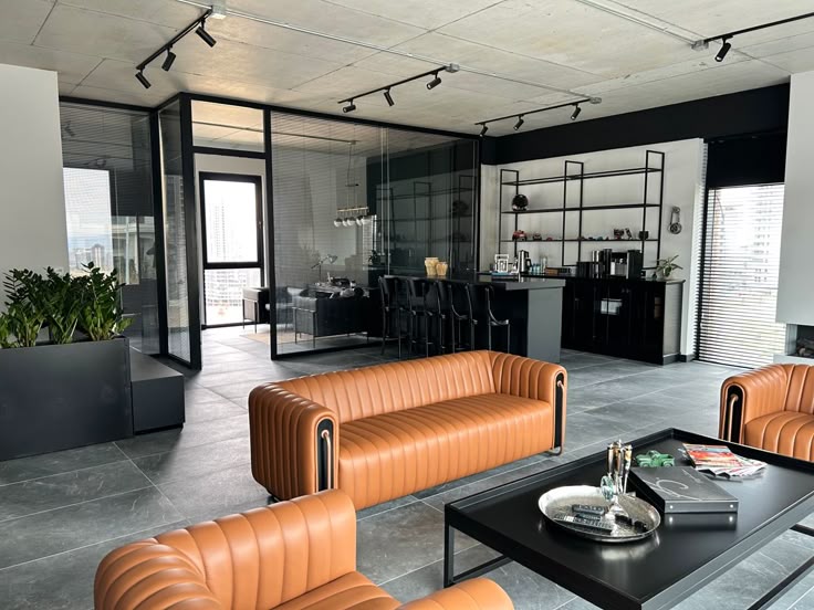 Modern office interior with brown leather sofas, glass-walled meeting room, and a sleek black bar area.