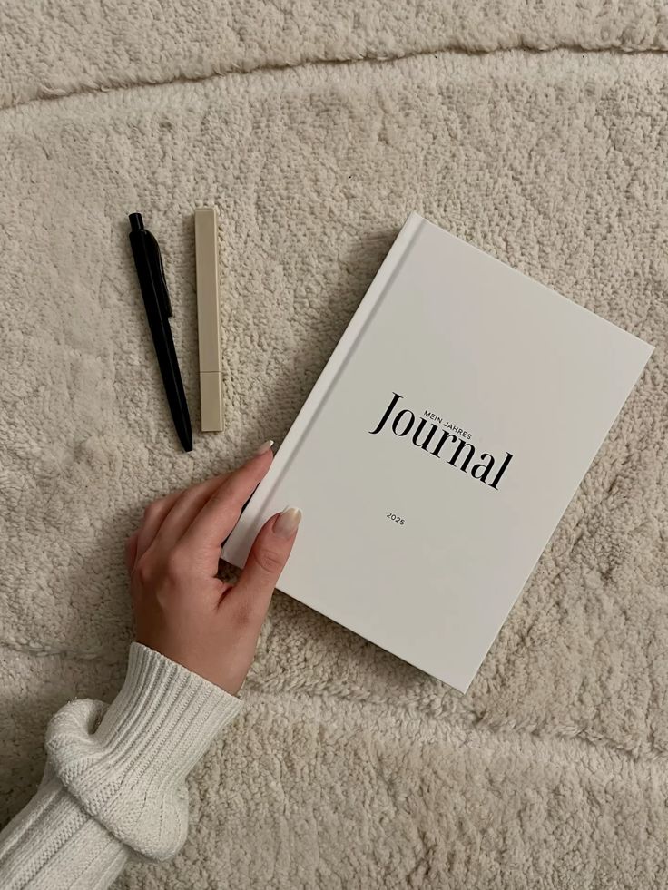 A white journal labeled Mein Jahres Journal 2023 with pens on a cozy beige blanket.
