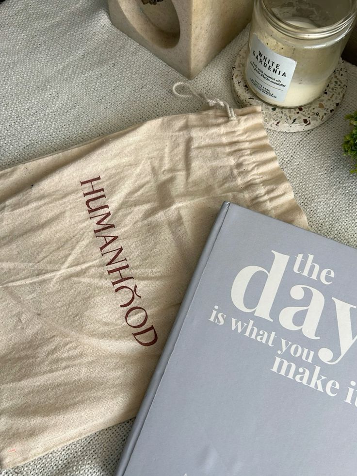 Neutral-toned book and cloth bag with a candle on linen surface.