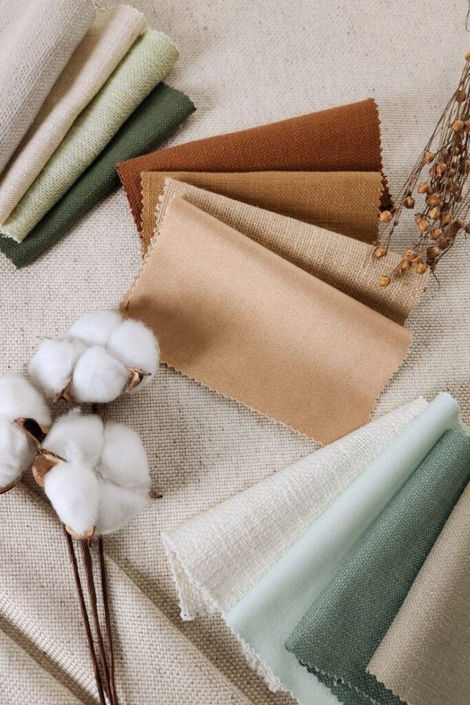 Fabric swatches in earthy tones with a cotton branch, showcasing natural textile options on a burlap backdrop.