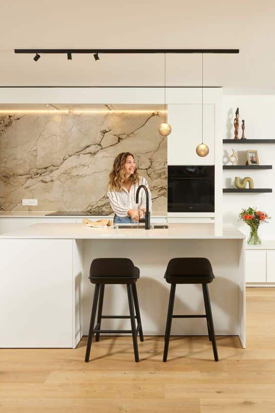 Keukens Modern kitchen with marble backsplash, island, woman smiling, black stools, pendant lights. Elegant and stylish design. | Sky Rye Design Modern kitchen with marble backsplash, island, woman smiling, black stools, pendant lights. Elegant and stylish design.