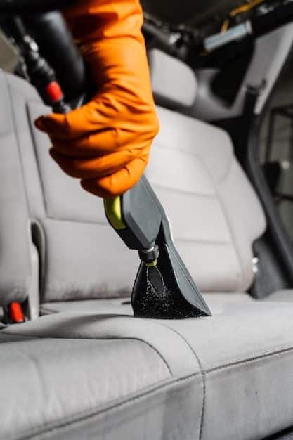 Vacuuming car seat with an upholstery cleaner to remove dirt, featuring an orange-gloved hand for professional detailing.