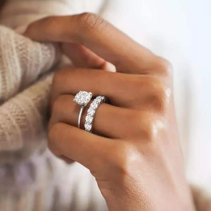 Close-up of a hand wearing a diamond engagement ring and eternity band, showcasing elegant jewelry.