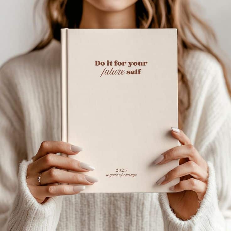 Woman holding a 2025 motivational journal with Do it for your future self on the cover, wearing a cozy sweater.