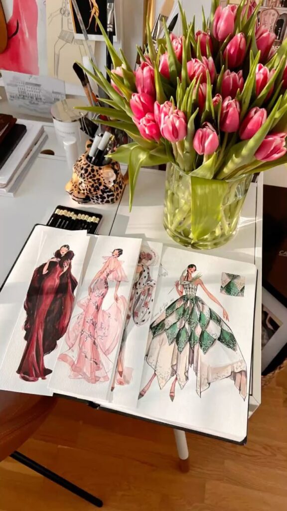 Fashion sketches and pink tulips on designer's desk.
