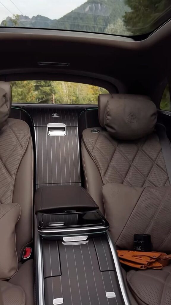 Luxury car interior featuring plush brown leather seats and scenic mountain views through a large sunroof.