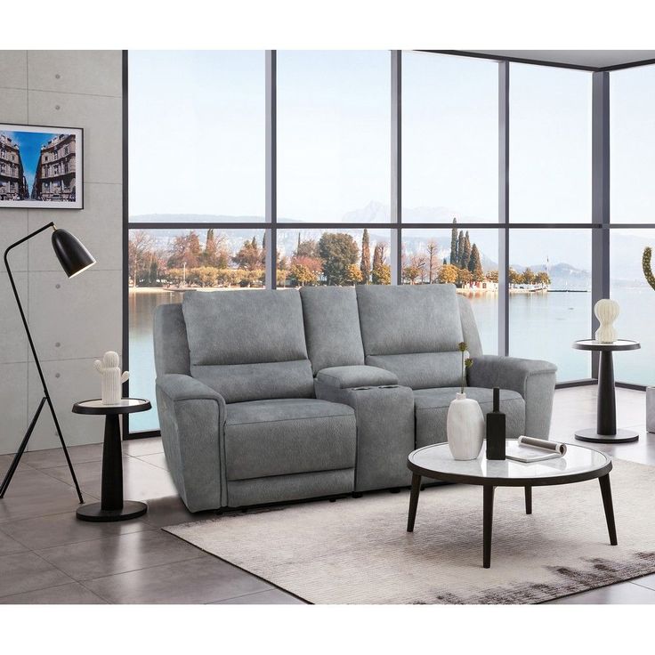 Modern living room with grey sectional sofa, stylish floor lamp, and scenic lake view through large windows.