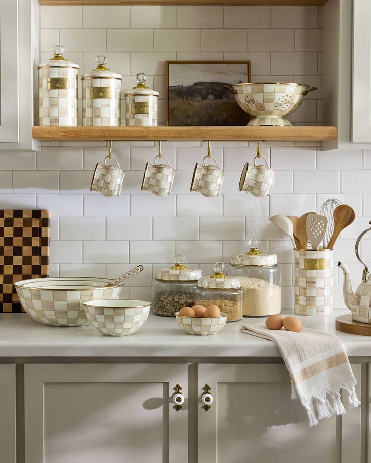 Elegant kitchen decor with checkered containers, mugs, and utensils on shelves against white tile backsplash.