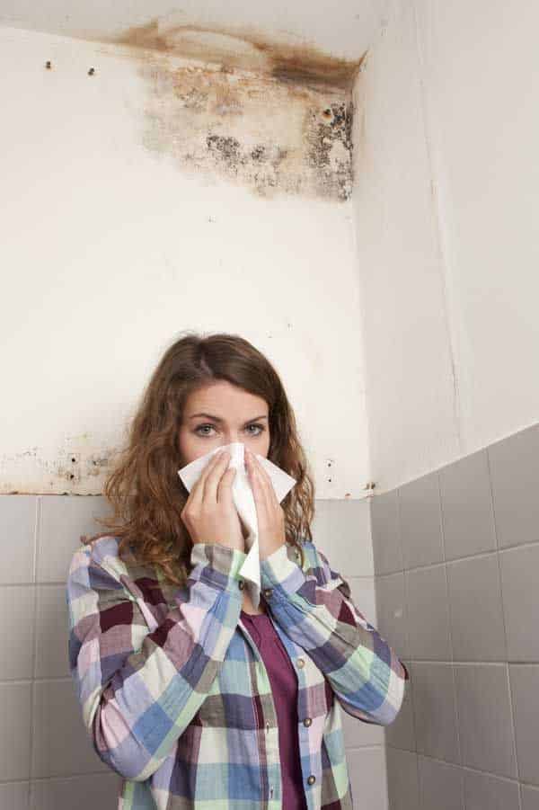 Woman with tissue reacting to mold on bathroom wall. Mold problem in home environment.