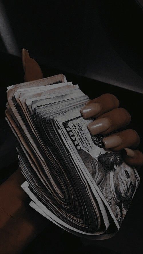 Hand holding a stack of U.S. dollar bills, symbolizing wealth and financial success.