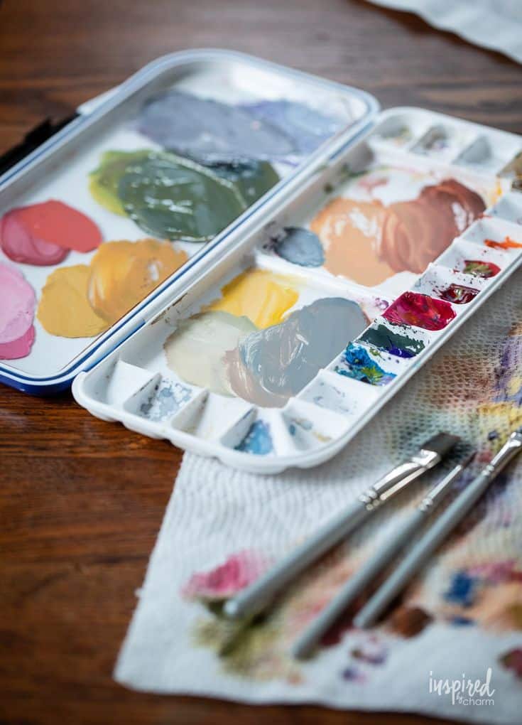 Artist's paint palette with colorful paints and brushes on a wooden table.