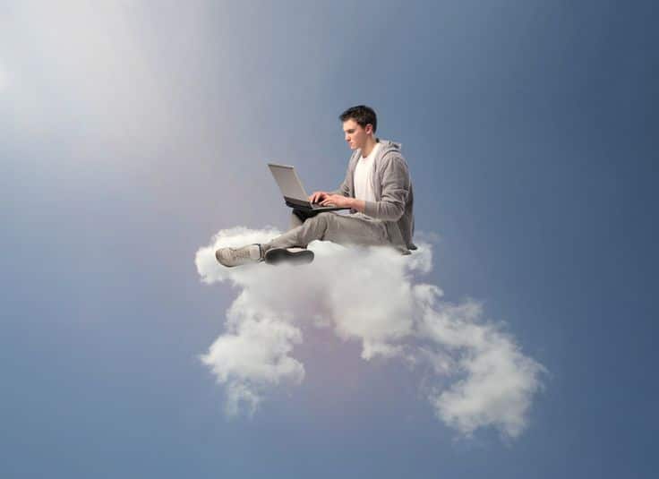 Man on a cloud using a laptop, symbolizing cloud computing and digital work in an open sky.