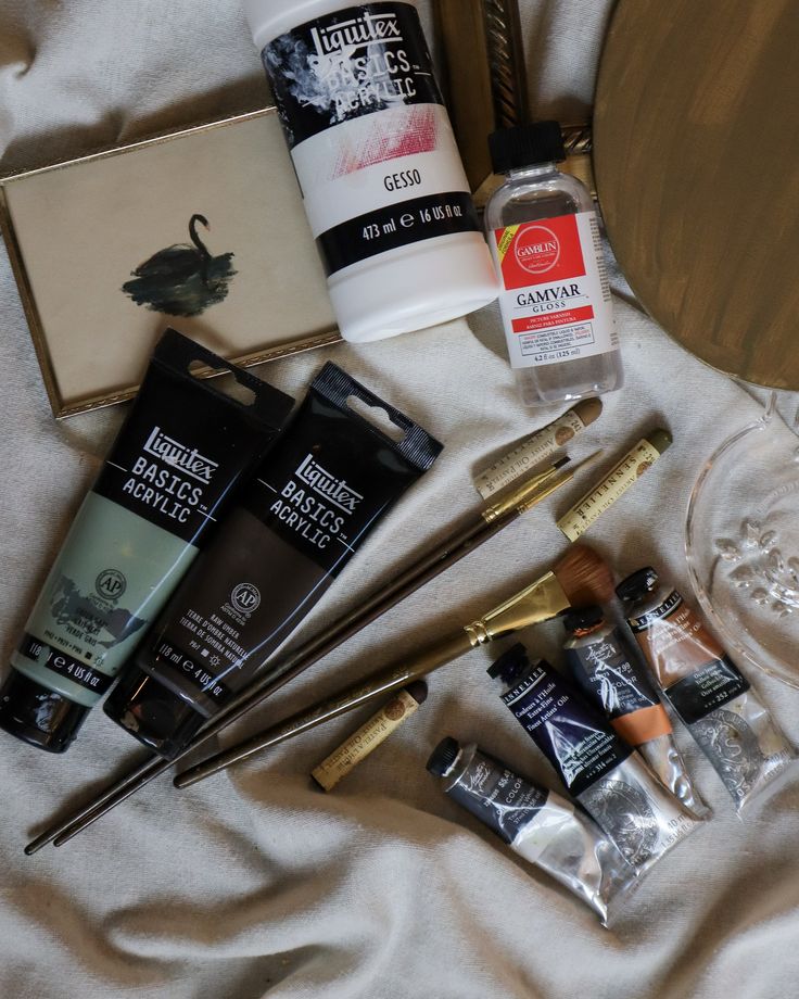 Art supplies assortment: acrylics, brushes, gesso, and gloss on canvas background for painting projects.