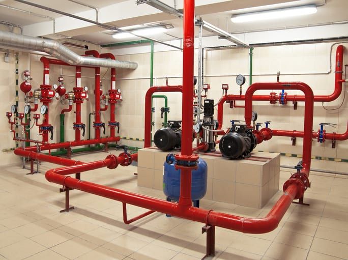 Red and green industrial pipe system with pumps in a utility room, featuring gauges and valves.