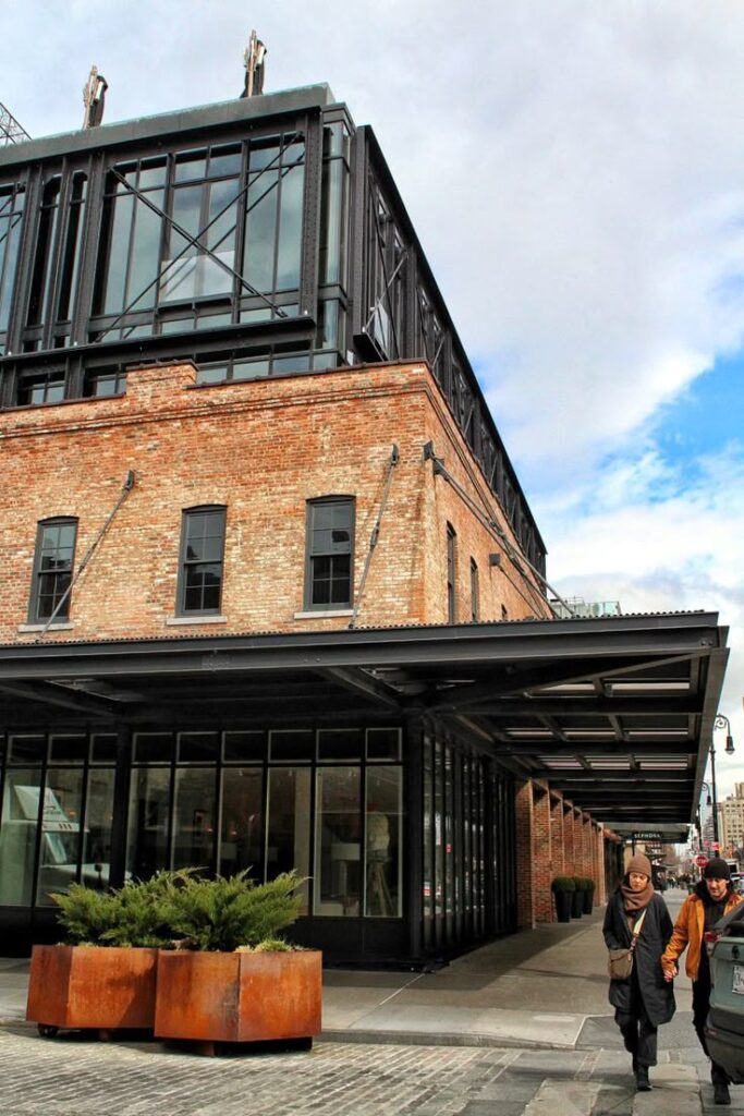 Modern industrial brick building with large windows and pedestrians walking on sidewalk under a cloudy sky.