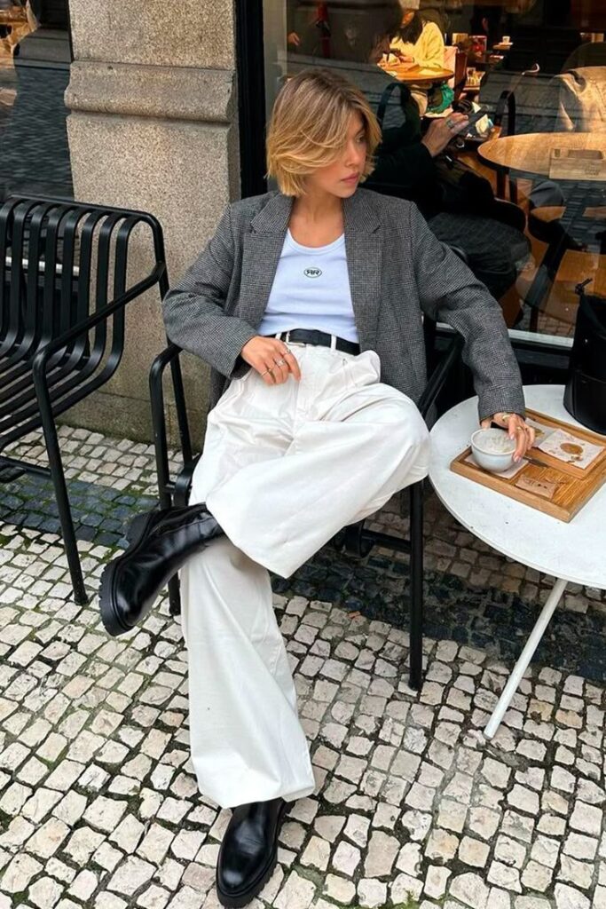 Stylish person in casual outfit enjoying a coffee at an outdoor café table on a cobblestone street.
