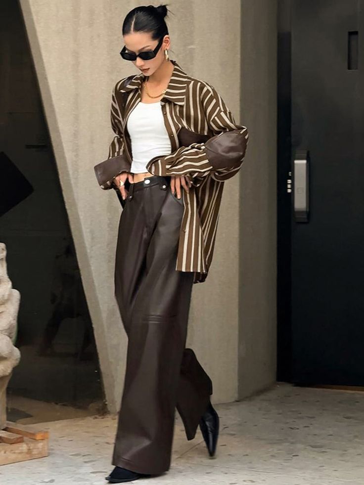 Fashionable woman in oversized striped shirt and leather pants, wearing sunglasses, exuding chic street style.