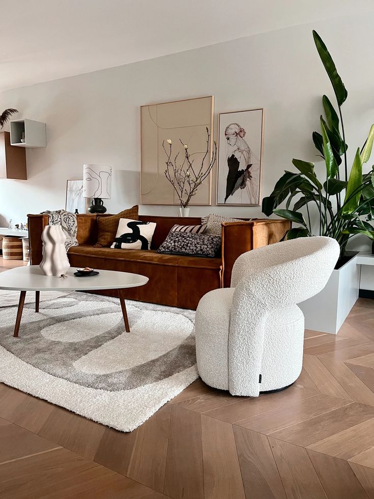 Modern living room with brown sofa, white armchair, abstract art, and lush plants, featuring a cozy rug and coffee table.