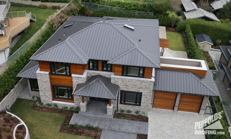 Modern house with a sleek metal roof, featuring wooden and stone accents in a landscaped yard.